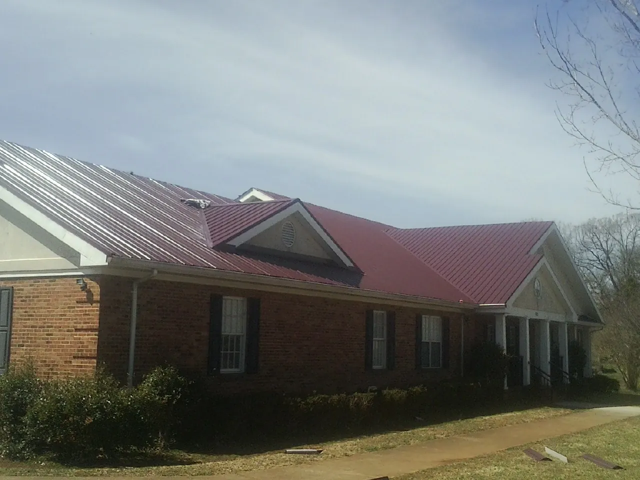 Red metal roof with gabled entries on a long brick building, from a Hail Damage Roof Repair job in Temple Hills