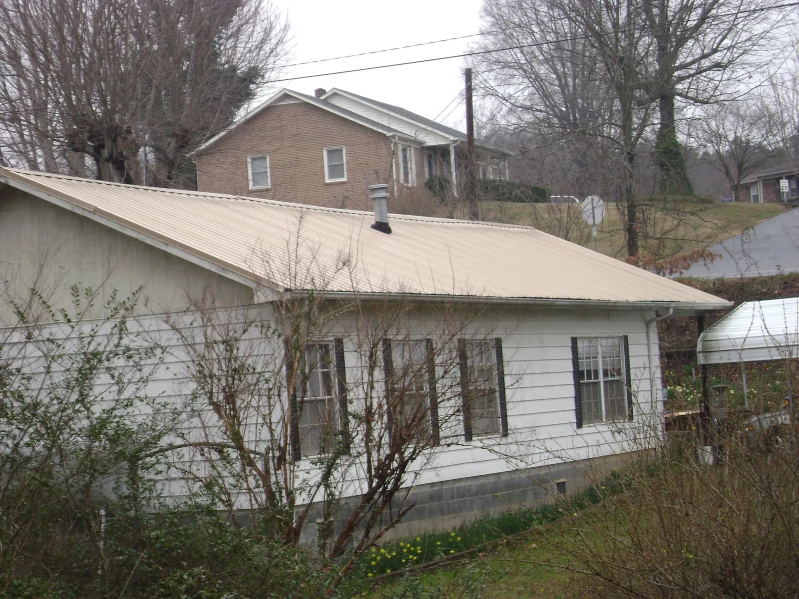Tan metal roof on a white sided house set into a hillside — Commercial Roofing by Roofing Brothers in Temple Hills