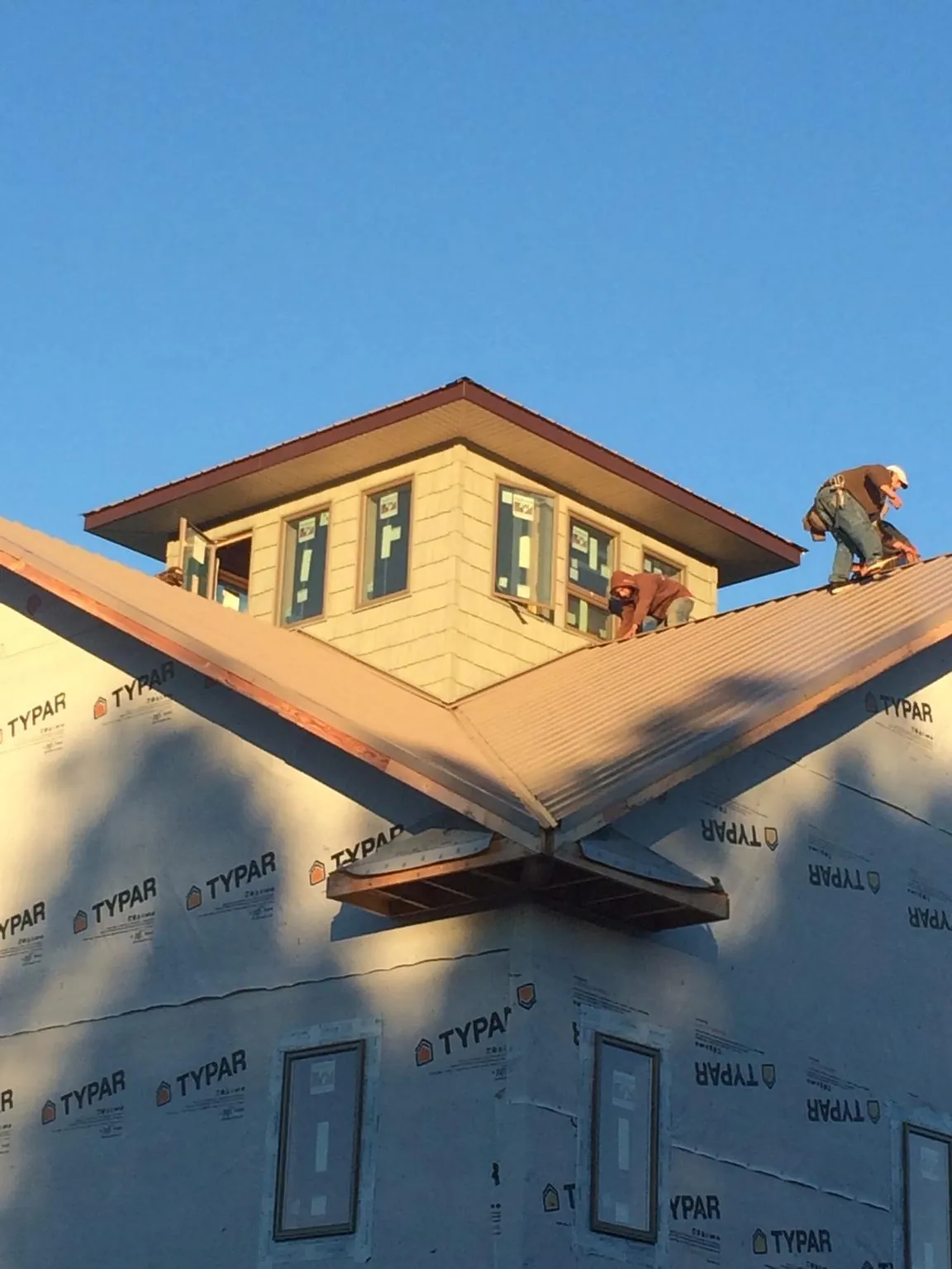 Roofers working around a rooftop cupola on a new metal roof at sunset — Roof Waterproofing in Temple Hills by Roofing Brothers